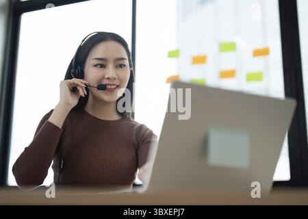 Ein professioneller Callcenter-Agent mit Headset, der in einem modernen Büro an einem Laptop arbeitet und den Kunden unterstützt Stockfoto