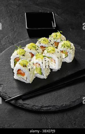 Frisch zubereitete Uamaki-Sushi-Brötchen werden auf einem schwarzen Schieferteller mit Lachs, Avocado und Frischkäse serviert, garniert mit Mikrogrün, SE Stockfoto