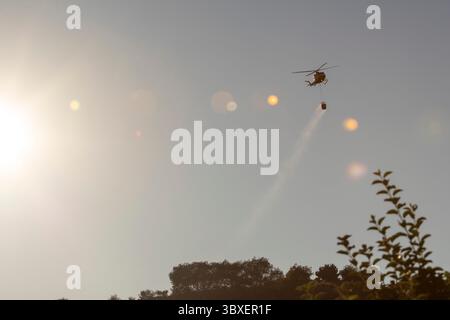 Allariz, Spanien, 16. Juli 2025: Ein gelb-schwarzer Feuerwehrhubschrauber fliegt am Himmel. Der Hubschrauber trägt einen Feuerwehrschlauch und fällt Stockfoto