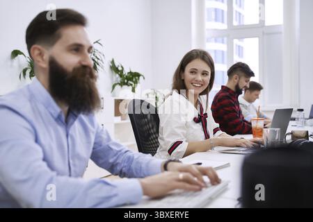 Menschen, die in modernen IT-Büros kommunizieren und arbeiten. Gruppe junger und erfahrener Programmierer und Softwareentwickler, die an Schreibtischen sitzen und an c Stockfoto