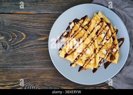 Zwei Pfannkuchen mit Schokoladensirup, Mandelflocken auf dem Teller, Honig fließt aus dem Löffel, Draufsicht, Kopierraum Stockfoto