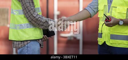 Nahaufnahme von zwei Personen in Sicherheitswesten, die die Hand schütteln, was die Zusammenarbeit in Logistik und Technik auf einer Baustelle darstellt Stockfoto