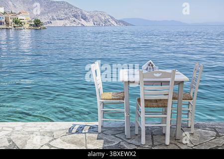 Weiße Stühle mit Tischen in typisch griechischer Taverne am Meer in Symi Stadt Stockfoto