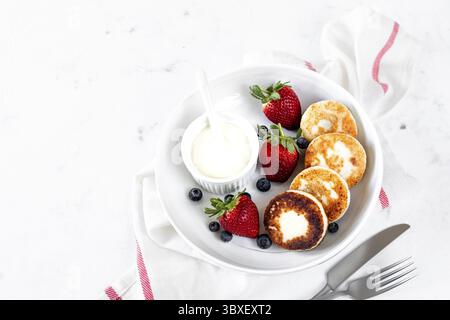 Essen, Hüttenkäsepfannkuchen, Käsekuchen, Ricotta-Krapfen mit frischen Erdbeeren und Heidelbeeren von einer weißen Keramikplatte. Gesund und lecker Stockfoto