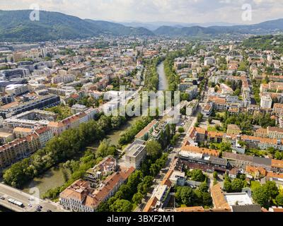 Aus der Vogelperspektive auf die Mur, die sich durch das Herz der Stadt schlängelt, gesäumt von grünen Bäumen, die sich von den Terrakotta-Dächern abheben, Graz, Steiermark, Österreich. Stockfoto