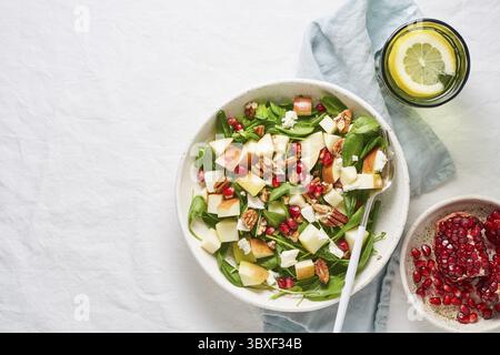 Obstsalat mit Nüssen, ausgewogenes Essen, sauberes Essen. Spinat mit Äpfeln, Pekannüssen und Feta, garniert mit Granatapfelkernen in einer Schüssel auf dem Tisch mit Weißwein Stockfoto