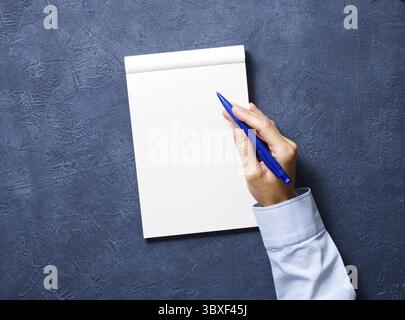Frau schreibt in Notizbuch auf einem dunkelblauen Tisch, Hand in Hemd mit Bleistift, Skizzenbuchzeichnung, Draufsicht Stockfoto