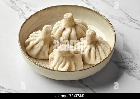 Traditionelle saftige georgianische hinkali-Knödel gefüllt mit gewürztem Hackfleisch, bestreut mit schwarzem Pfeffer, präsentiert auf gesprenkelter Keramikplatte Stockfoto