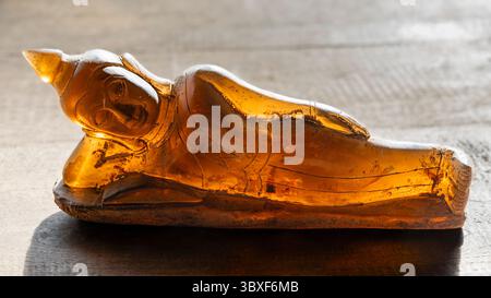 Nahaufnahme der wunderschönen, lichtdurchlässigen buddha-Statue aus braunem Kristall mit Hintergrundbeleuchtung auf hellem hölzernem Hintergrund Stockfoto