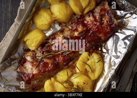 Scharfe Schweinerippchen vom Grill und zerstoßene Kartoffeln. Langsames Kochen. Gebratenes Schweinefleisch auf Folie im Tablett Stockfoto