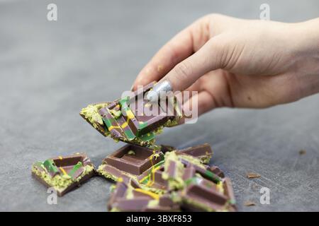 Die Hand der Frau hält ein Stück Dubai-Schokolade auf grauem Hintergrund. Grüner Kadayif und Pistazien mit Pistazien im Trenddessert. Nahaufnahme, selektiv Stockfoto