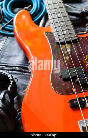 Orange E-Bass Gitarre, Kopfhörer und Kabel auf schwarzem Ledermantel Hintergrund. Stockfoto