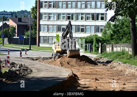 Bagger arbeiten im Sommer auf städtischen Straßenbaustellen. Erdbewegungsgeräte bereiten die Basis für neue Straßen vor, während Verkehrsschilder Fahrzeuge lenken. Inf Stockfoto