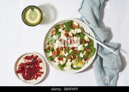 Obstsalat mit Nüssen, ausgewogenes Essen, sauberes Essen. Spinat mit Äpfeln, Pekannüssen und Feta, garniert mit Granatapfelkernen in einer Schüssel auf dem Tisch mit Weißwein Stockfoto