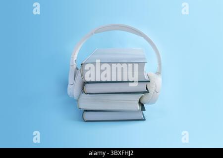 Kabellose weiße Kopfhörer auf einem Stapel Bücher auf hellblauem Hintergrund. Konzept für Hörbücher im minimalen Stil Stockfoto