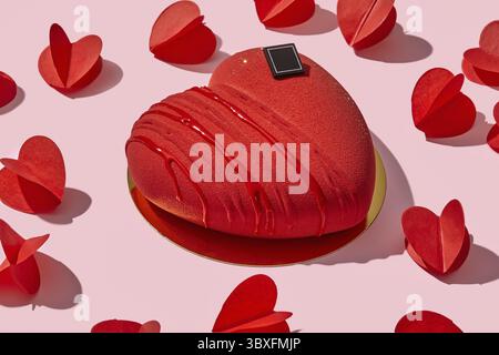 Kräftiger roter, samtförmiger Mousse-Kuchen in Herzform, präsentiert auf goldener Plattform, inmitten verstreuter Papierherzen auf zartem rosa Hintergrund. Perfekt für Romantik Stockfoto