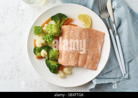 Dampflachs und Gemüse, Paleo, Keto, Fodmap, DASH-Diät. Mediterrane Ernährung mit gedämpftem Fisch. Gesundes Konzept, weiße Platte auf grauem Tisch, Gluten Stockfoto