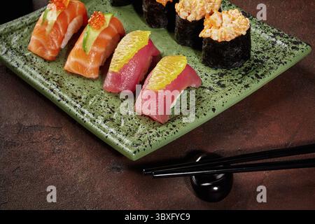 Frisch zubereitetes Sushi-Sortiment mit Thunfisch, Lachs und anderen Zutaten, serviert auf grünem Teller mit Essstäbchen Stockfoto