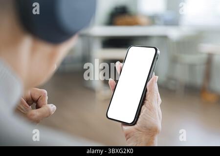 Nahaufnahme einer älteren Frau, die ein Smartphone mit einem leeren Bildschirm hält, zu Hause sitzt und sich auf die Hand und das Gerät konzentriert Stockfoto