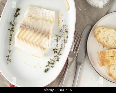 Kabeljaufischfilet, frisch im Ofen mit Thymian zum Backen in einer Porzellanschale gekocht, Brot auf einem Teller, Draufsicht Stockfoto