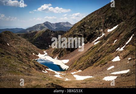 Eine atemberaubende Berglandschaft mit einem ruhigen blauen See, umgeben von felsigem Gelände und Schneeflächen. Die Szene fängt die raue Schönheit ein Stockfoto
