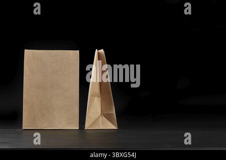 Umweltfreundliches Einweggeschirr. Zwei biologisch abbaubar, braun Handwerk Papiertüten auf eine dunkle Oberfläche vor einem schwarzen Hintergrund. Recycling Konzept. Auch verwenden Stockfoto