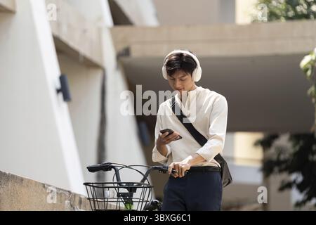 Moderne Pendelfahrt und digitale Konnektivität. Ein junger Mann überprüft sein Handy, während er auf seinem Fahrrad parkt, und genießt einen Moment der technischen Entspannung Stockfoto