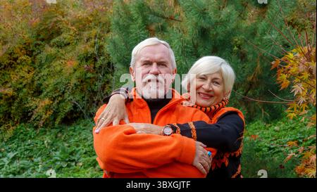 Älteres grauhaariges optimistisches Ehepaar Mann und Frau im Herbst in orangefarbenen Pullis Stockfoto