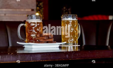 Zwei Gläser helles Bier stehen auf einem Tisch in einer Bierbar, daneben sind salzige, getrocknete Croutons aus Schwarzbrot. Stockfoto
