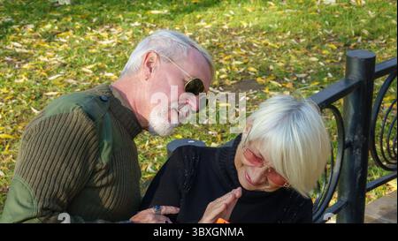 Porträt eines älteren grauhaarigen Paares, eines Mannes in Khaki-Militärkleidung, einer Frau in einem schwarzen Pullover, mit einem orangen Smartphone Stockfoto