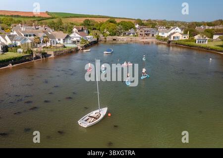 Aus der Vogelperspektive gleiten Paddelboarder über das ruhige Wasser in der Nähe der Stadt, umgeben von malerischen Gebäuden und üppigem Grün, Kingsbridge, England, Großbritannien. Stockfoto