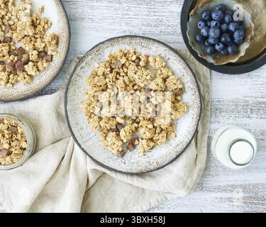 Joghurt mit Schokoladengranola, Heidelbeere. Frühstück, gesunde Ernährung mit Haferflocken, Nüssen, Banane, rustikaler Holztisch, Blick von oben Stockfoto