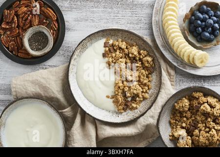 Joghurt mit Schokoladengranola, Heidelbeere. Frühstück, gesunde Ernährung mit Haferflocken, Nüssen, Banane, rustikaler Holztisch, Blick von oben Stockfoto