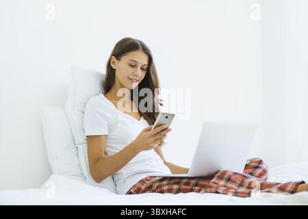 Junge Frau, die online einkaufen, Code aus SMS-Nachricht auf dem Handy eingeben, Sicherheit beim Online-Shopping. Frau, die auf dem Bett im Schlafzimmer sitzt und arbeitet Stockfoto