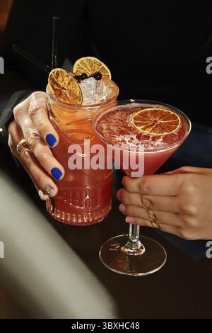 Zwei Frauen halten erfrischende Tiki-Cocktails, garniert mit getrockneten Orangenscheiben und Eiswürfeln Stockfoto