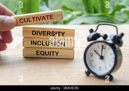 Pflegen Sie Text für Vielfalt, Inklusion und Gerechtigkeit auf Holzblöcken mit verschwommener Tischuhr. D- und I-Konzept Stockfoto