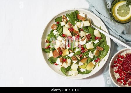 Obstsalat mit Nüssen, ausgewogenes Essen, sauberes Essen. Spinat mit Äpfeln, Pekannüssen und Feta, garniert mit Granatapfelkernen in einer Schüssel auf dem Tisch mit Weißwein Stockfoto