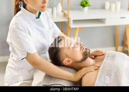 Ruhiger Mann, der auf dem Tisch liegt und eine Schulter- und Nackenmassage vom weiblichen Masseur erhält Stockfoto