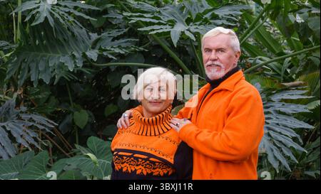Fröhliche positive ältere Paare in einem botanischen Garten unter grünen exotische Pflanzen in helle Kleidung Stockfoto