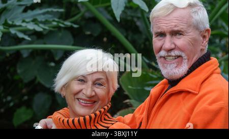 Fröhliche positive ältere Paare in einem botanischen Garten unter grünen exotische Pflanzen in helle Kleidung Stockfoto