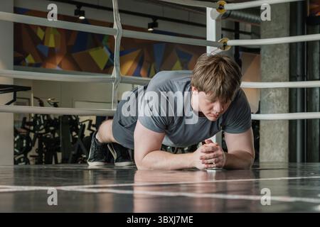 Junge kaukasische männliche Person in grauer Sportbekleidung ist Plank-Position im Fitnessstudio. Fitnessstudio. Gesundheit und Training. Stockfoto