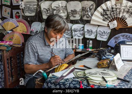 18. Mai 2013, Wuzhen, Provinz Zhejiang, China: Ein Chinese malt traditionelle Szenen über Fans in seinem Geschäft in Wuzhen, China. (Kreditbild: © Jon G. Fuller/VW Pics via ZUMA Press Wire) Stockfoto