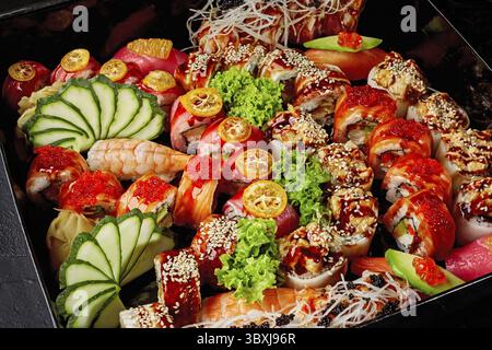 Nahaufnahme eines großen Sets köstlicher Brötchen und Nigiri-Sushi mit Lachs, Thunfisch, Aal und Garnelen garniert mit Gari, Obst, Gemüse und Gemüse in Blac Stockfoto