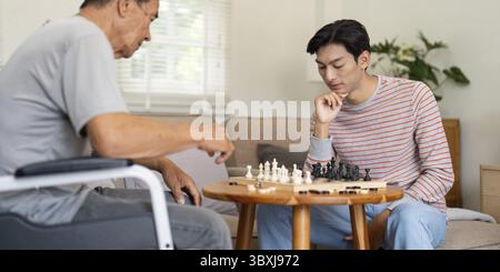 Ein Sohn konzentrierte sich auf seinen nächsten Schachzug mit seinem Vater, der im Rollstuhl sitzt, und zeigte seine enge Familienbindung in der Freizeit Stockfoto