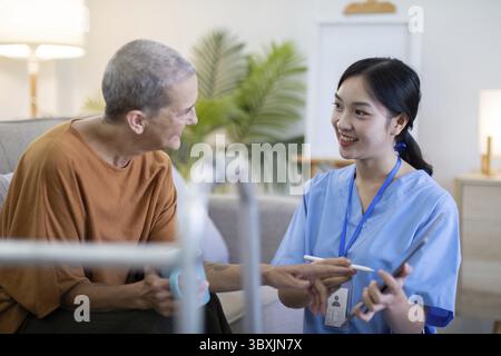 Asiatische Pflegekraft, die ein digitales Tablet mit einer älteren Frau zu Hause verwendet, wobei die Pflege älterer Menschen und der Einsatz digitaler Gesundheitstools hervorgehoben werden Stockfoto