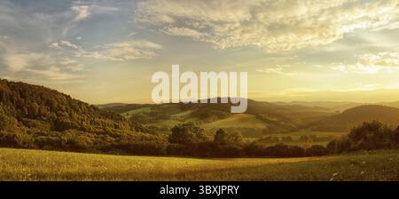 Sonnenuntergang über hügeliger Landschaft, das goldene Leuchten der untergehenden Sonne, Wiese im Vordergrund Stockfoto