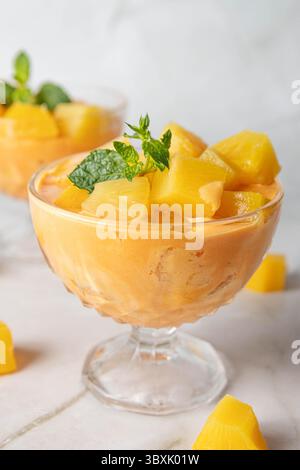 Zwei Tassen mit appetitlich gelbem Eis mit Mango, Ananas, Kantaloupe Geschmack, gekrönt mit Ananasstücken, dekoriert mit einem kleinen Minzblatt Stockfoto