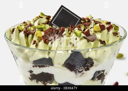 Nahaufnahme mit köstlichen, mehrschichtigen Kleinigkeiten mit Brownie-Stücken, Pistazieneis und Schlagsahne garniert mit Schokoladenspänen und Nüssen serviert Stockfoto
