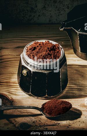 Gemahlener Kaffee, bereit zum Brühen in einem italienischen Mokakopffilter, bereit zum Brühen, mit einem Löffel auf einem Holztisch und warmem Licht Stockfoto