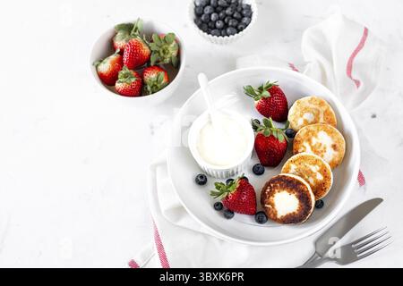 Essen, Hüttenkäsepfannkuchen, Käsekuchen, Ricotta-Krapfen mit frischen Erdbeeren und Heidelbeeren von einer weißen Keramikplatte. Gesund und lecker Stockfoto